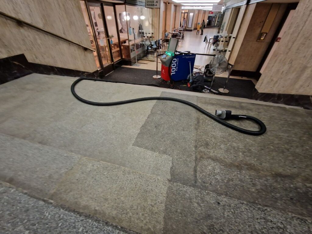 Pohled na žulové schodiště čištěné pomocí mobilního čisticího zařízení, ukazující kontrast mezi čištěnými a nečištěnými oblastmi.